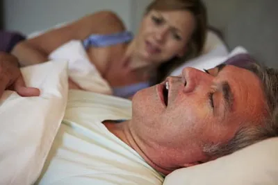 woman awake at night while her husband snores due to sleep apnea